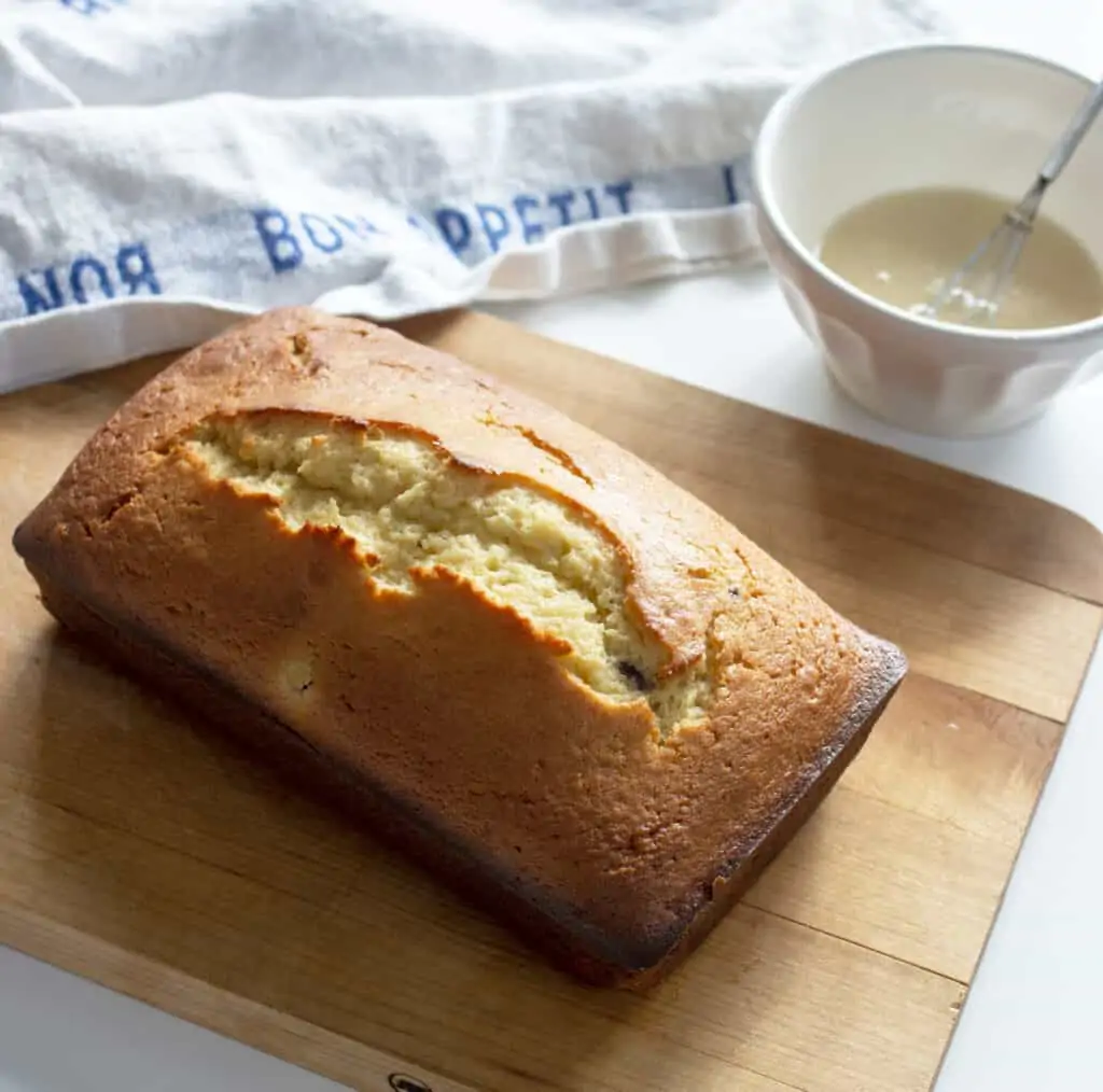 lemon yogurt cake in a slicing board with white bowl and cloth