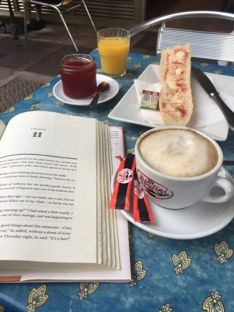 an open book, coffee, jam and bread on a table 